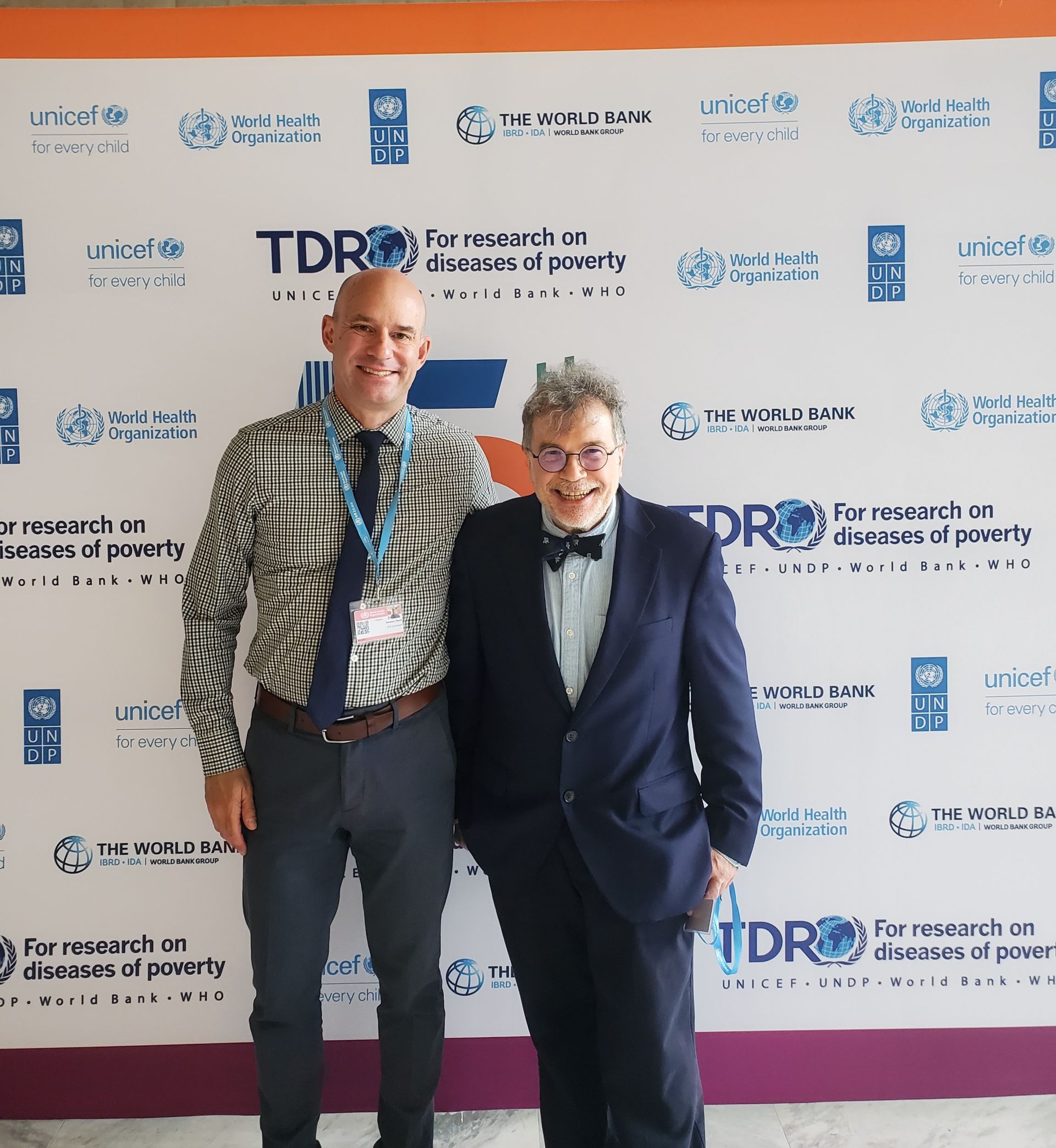 Dr. Diemert and colleague smiling in front of the TDR step and repeat banner 