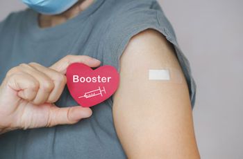 A person holding a heart-shaped card labeled 'Booster' with a syringe icon next to their arm with a bandage
