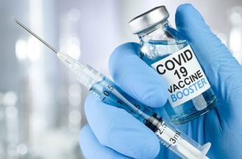 A gloved hand holding a COVID-19 vaccine booster vial and syringe